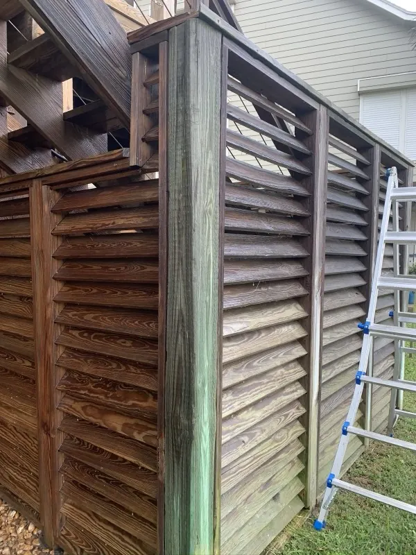 Before: mildewed gray-green louvered fence mid-wash, ladder beside it