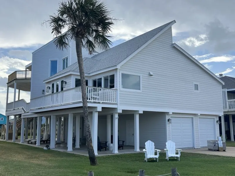White raised beach house on Galveston Island with a palm tree and a freshly cut lawn